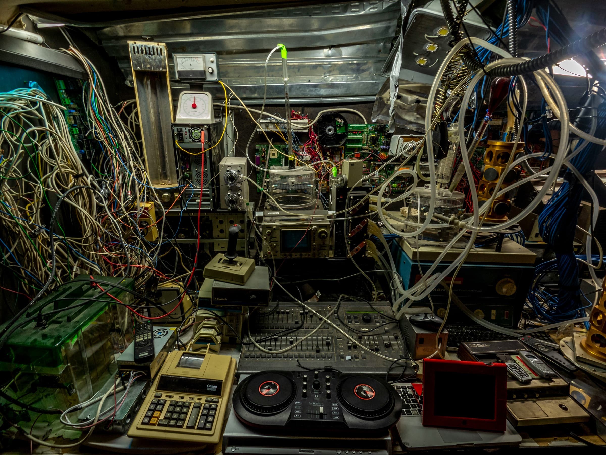 A workbench crammed with old electronics, joined by a tangle of wires and tubes