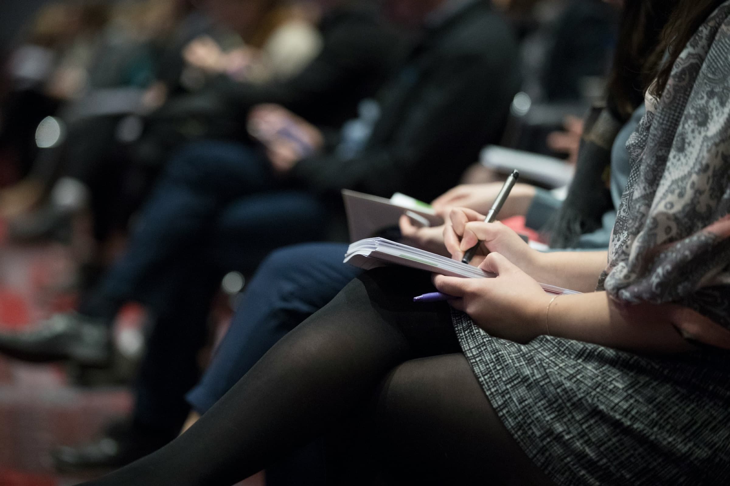 People in a lecture audience writing in notebooks